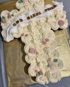 cake in the shape of a cross, with "God Bless Priya" written on it.